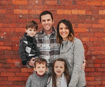 young missionary couple standing against a red brick wall