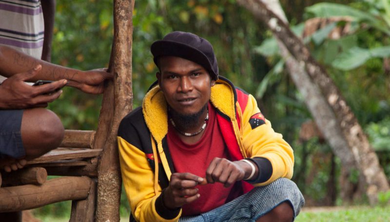 Mouk Man crouching by house