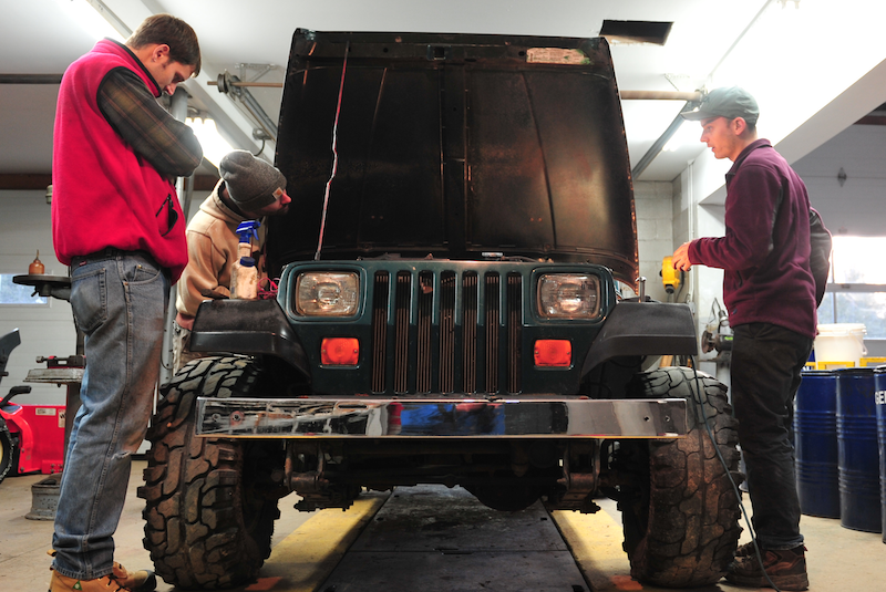 some guys looking under the hood of a vehicle in a shop