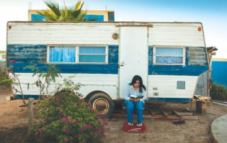 woman reading Bible while sitting on step of her camper trailer