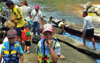 kids and adults on a river bank preparing for a canoe trip