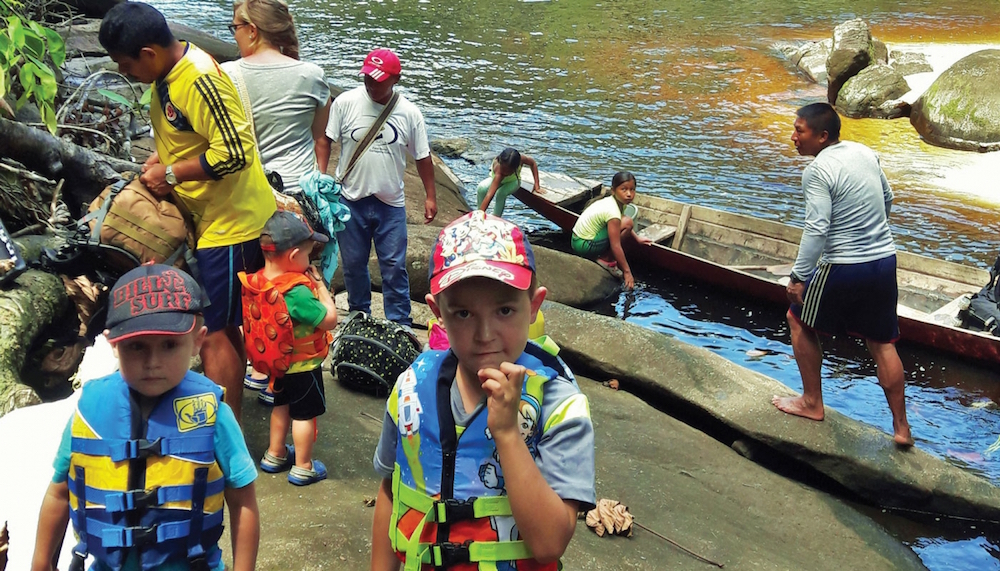 kids and adults on a river bank preparing for a canoe trip