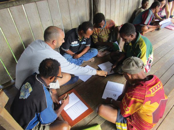 missionary helps tribal men practice their reading