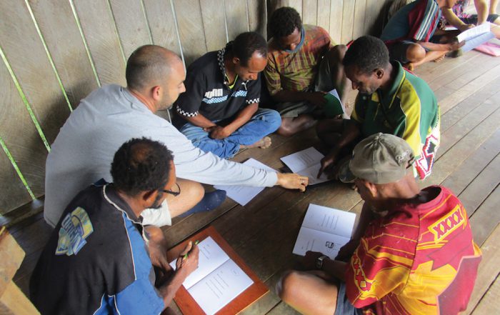 missionary helps tribal men practice their reading