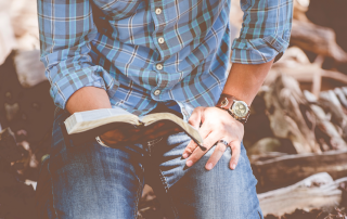 man kneeling on ground and holding Bible