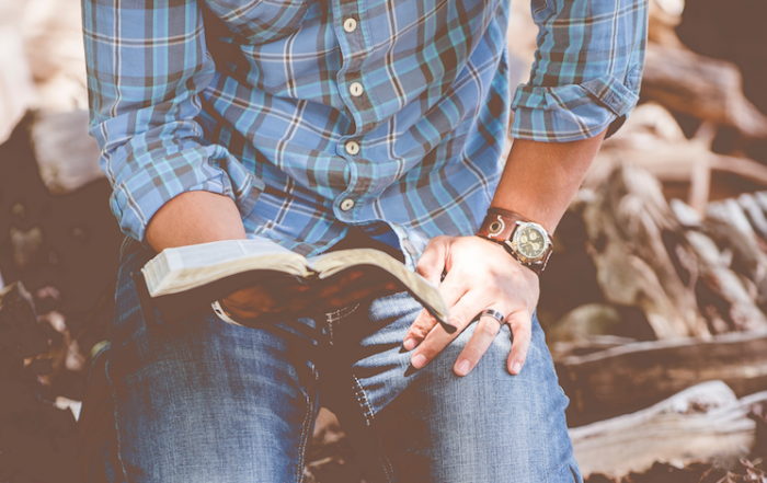 man kneeling on ground and holding Bible