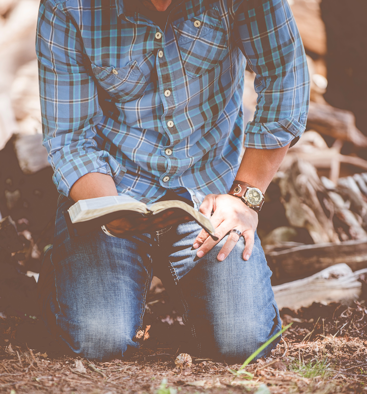 man kneeling on ground and holding Bible