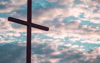 empty cross with a cloudy sunset sky in the background