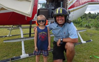 helicopter pilot with child wearing glasses and headphones beside a helicopter