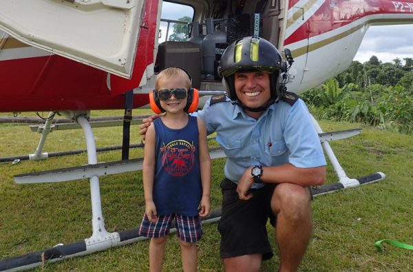 helicopter pilot with child wearing glasses and headphones beside a helicopter