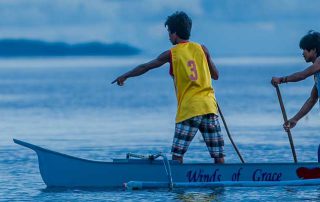 two men standing in an outrigger canoe