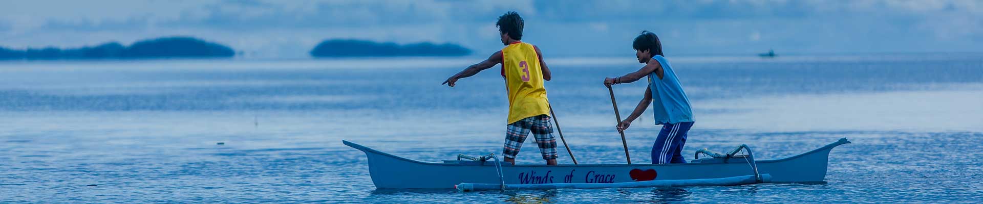 two men standing in an outrigger canoe