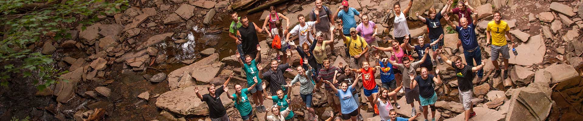 a bunch of wayumi participants on the edge of a rocky stream bed waving something up above them