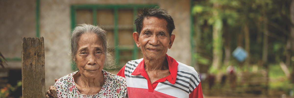 smiling couple with house and trees behind them
