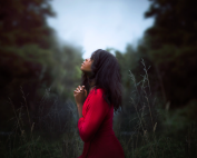 woman clasping her hands in prayer while standing in a clearing