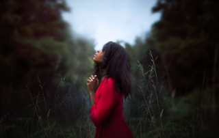 woman clasping her hands in prayer while standing in a clearing