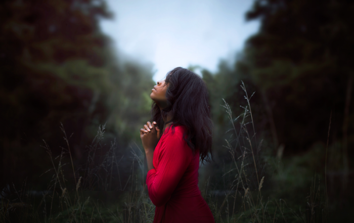 woman clasping her hands in prayer while standing in a clearing