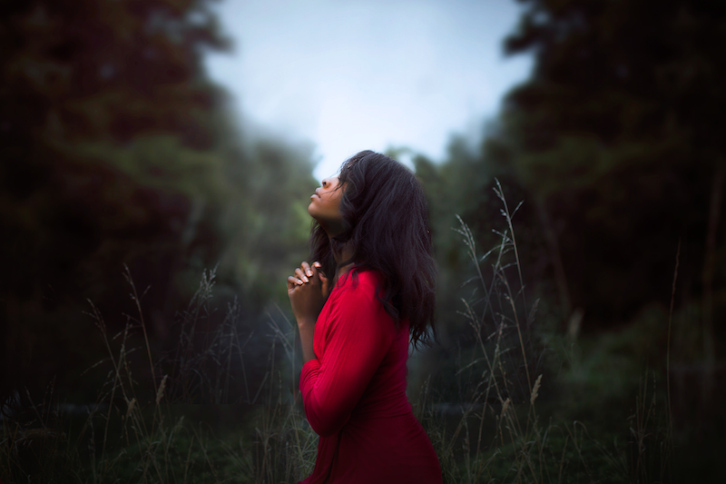 woman clasping her hands in prayer while standing in a clearing